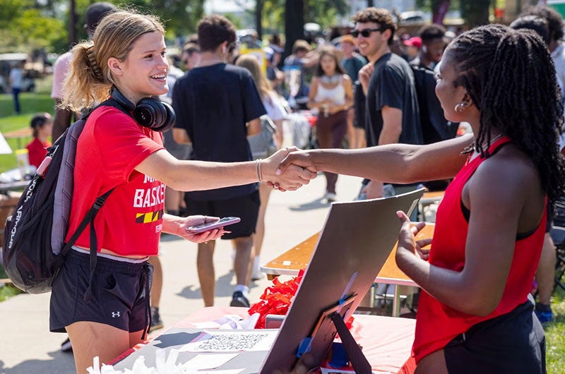 Two students shake hands and smile at the First Look Fair on McKeldin Mall.