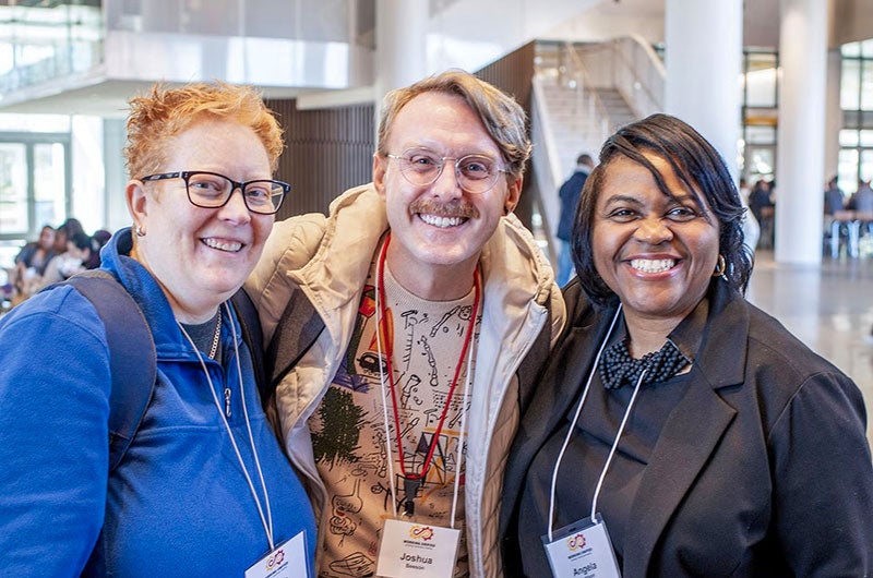 Three smiling colleagues wearing name tags pose together at a professional development event.