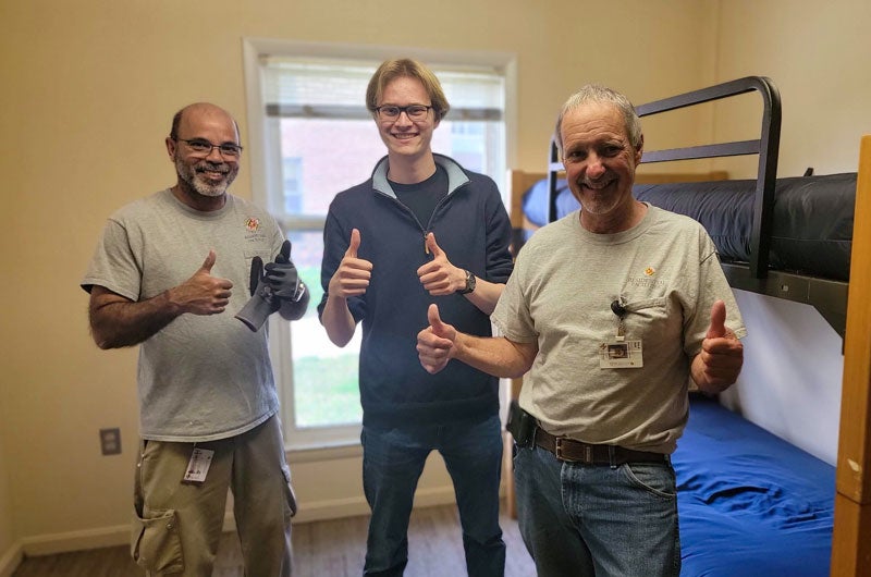 Two residential facilities staff and a student show thumbs up after bunking beds in a residence hall room.