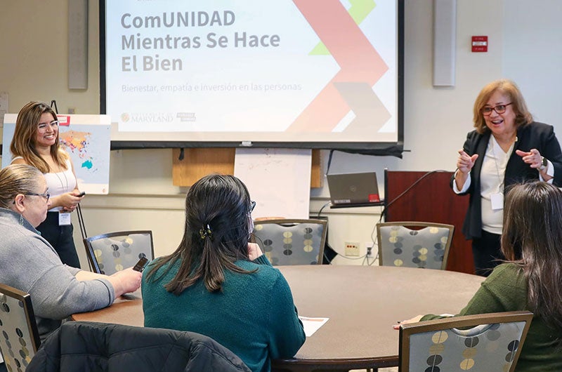 A presenter stands at a podium next to a screen showing a Spanish-language presentation.