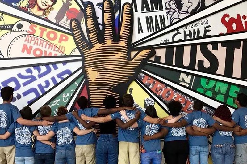 Students with their backs to the camera facing a colorful wall mural.