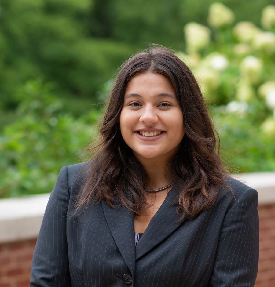 Woman smiling in a suit in front of plants and shrubbery