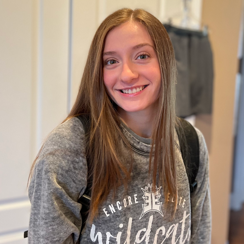 Young woman smiling and wearing a sweater that reads "wildcats"