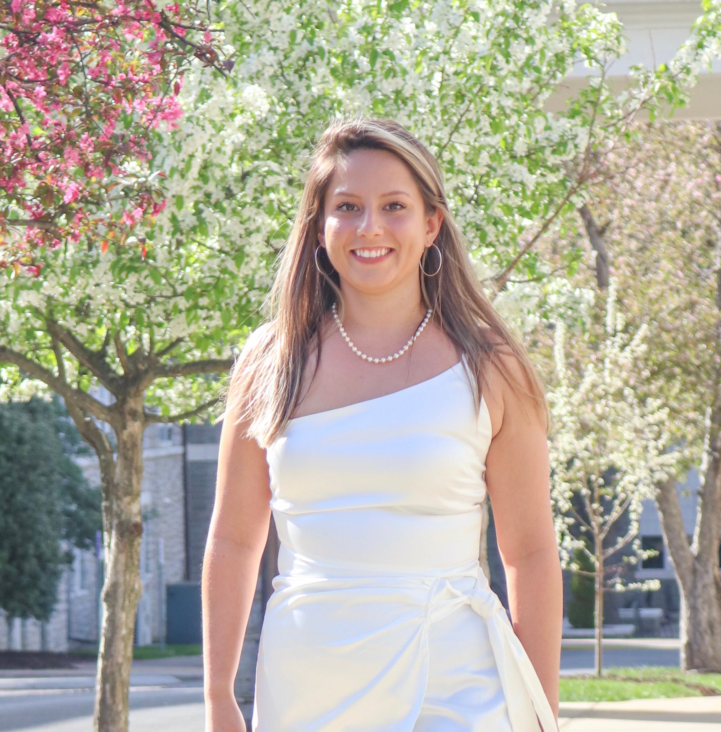 Woman wearing a dress and smiling in front of trees