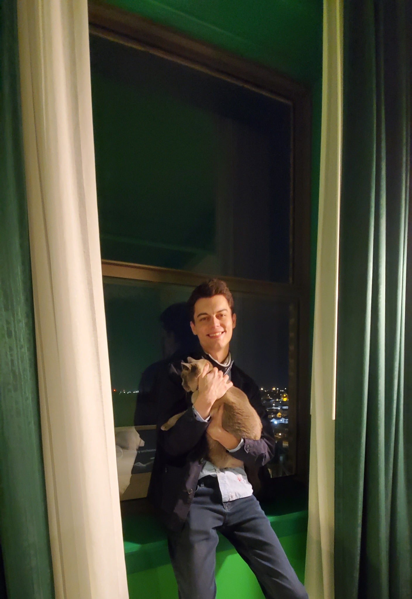 Man leaning up against a window and holding a cat