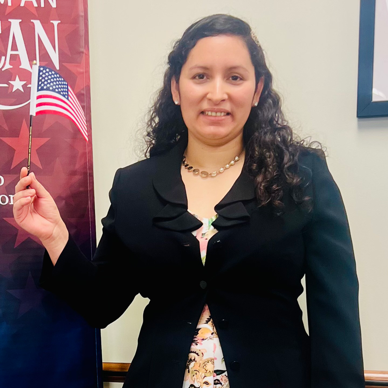 Woman smiling and wearing a suit while also holding a small American flag in her hand
