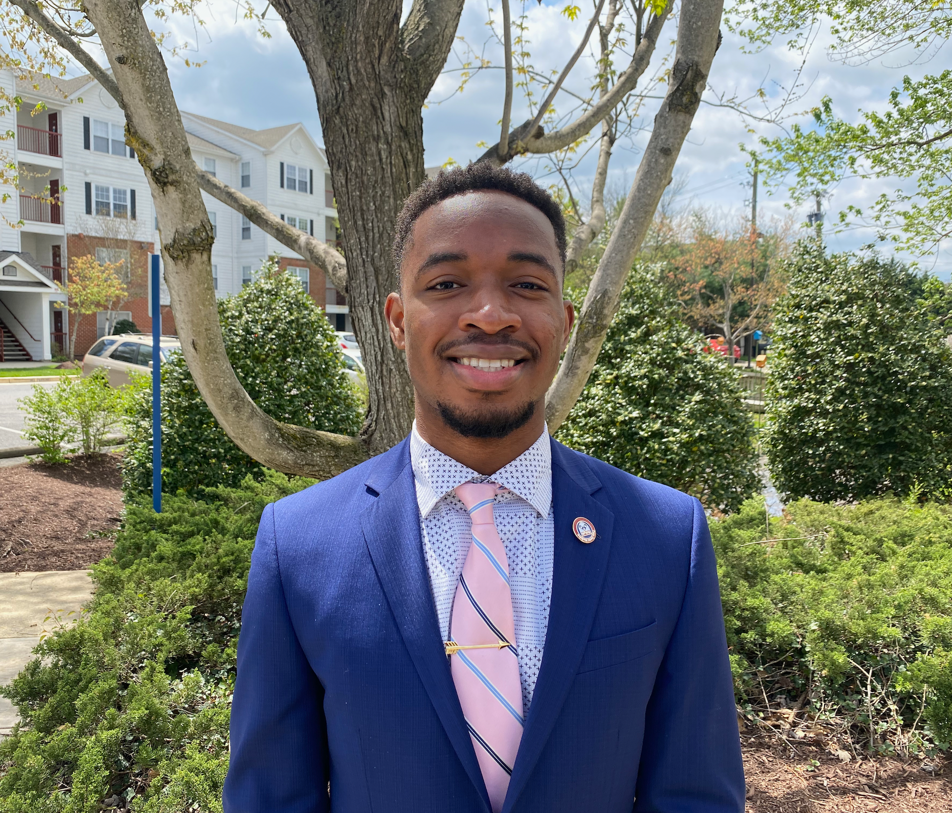 Young man smiling in a suit, in front of a tree