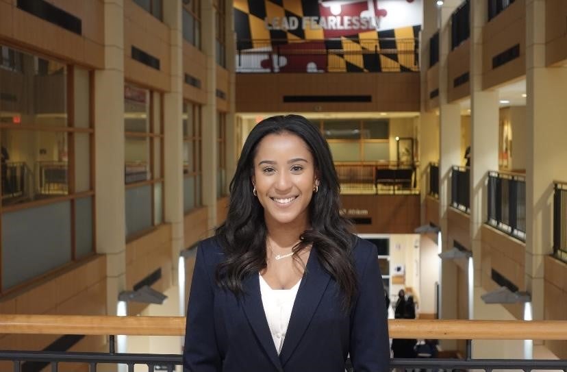 Woman smiling in a suit with the Maryland flag in the background