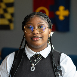 Young woman with glasses wearing necklaces in a professional outfit.