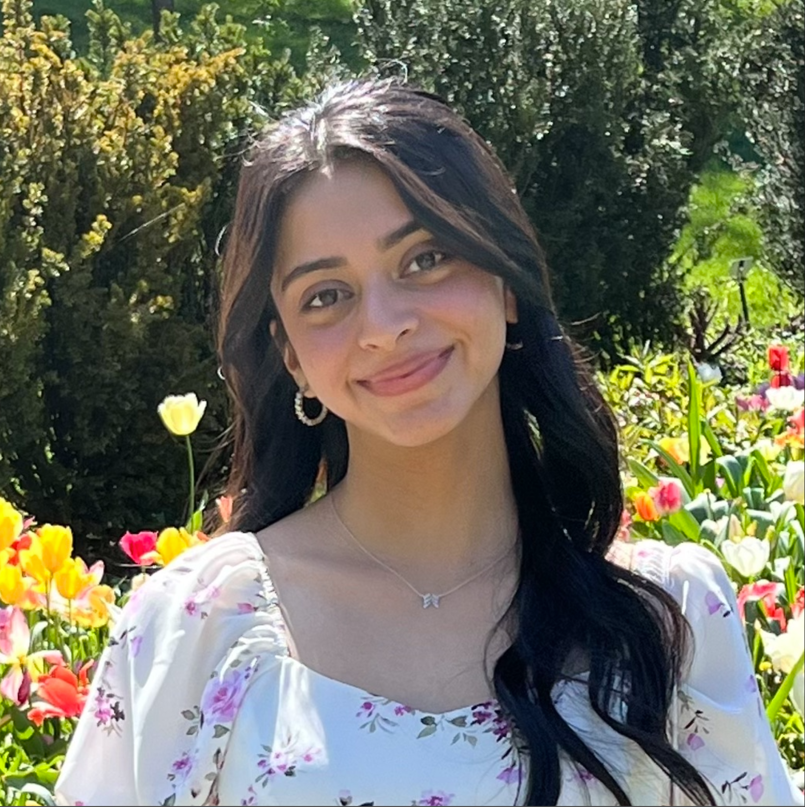 Young woman with a soft smile in front of flowers and other shrubbery