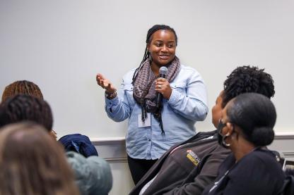 A staff member with a microphone talks to an audience of other staff