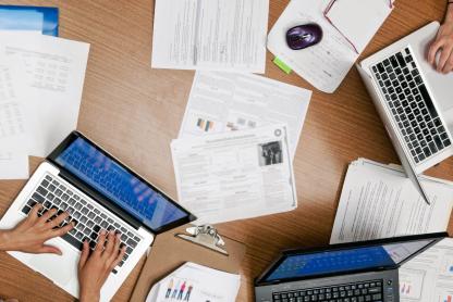 an overhead view of three computers on a desk with paper scattered around