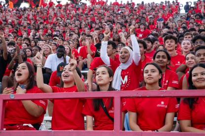 A large crowd of students in red Maryland shirts cheers enthusiastically from the stadium bleachers.