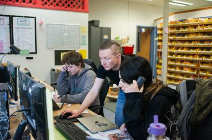 Three staff members work at a service desk with computers, phones, and many yellow mail slots.