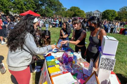 Students interact at a colorful information table during a busy First Look Fair on a sunny lawn.