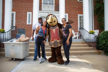 Testudo with a family in front of one of the brick houses on the row.