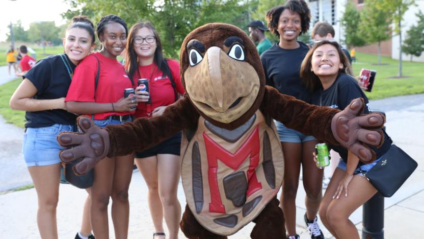 Students gather around and smile with Testudo, who has his arms open wide