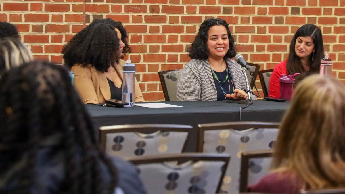 Staff members sit at a table and speak with other staff during a presentation