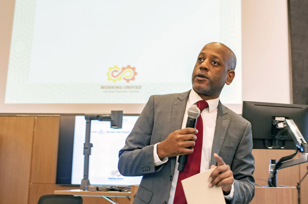 A staff member with a microphone talks with other staff during a presentation