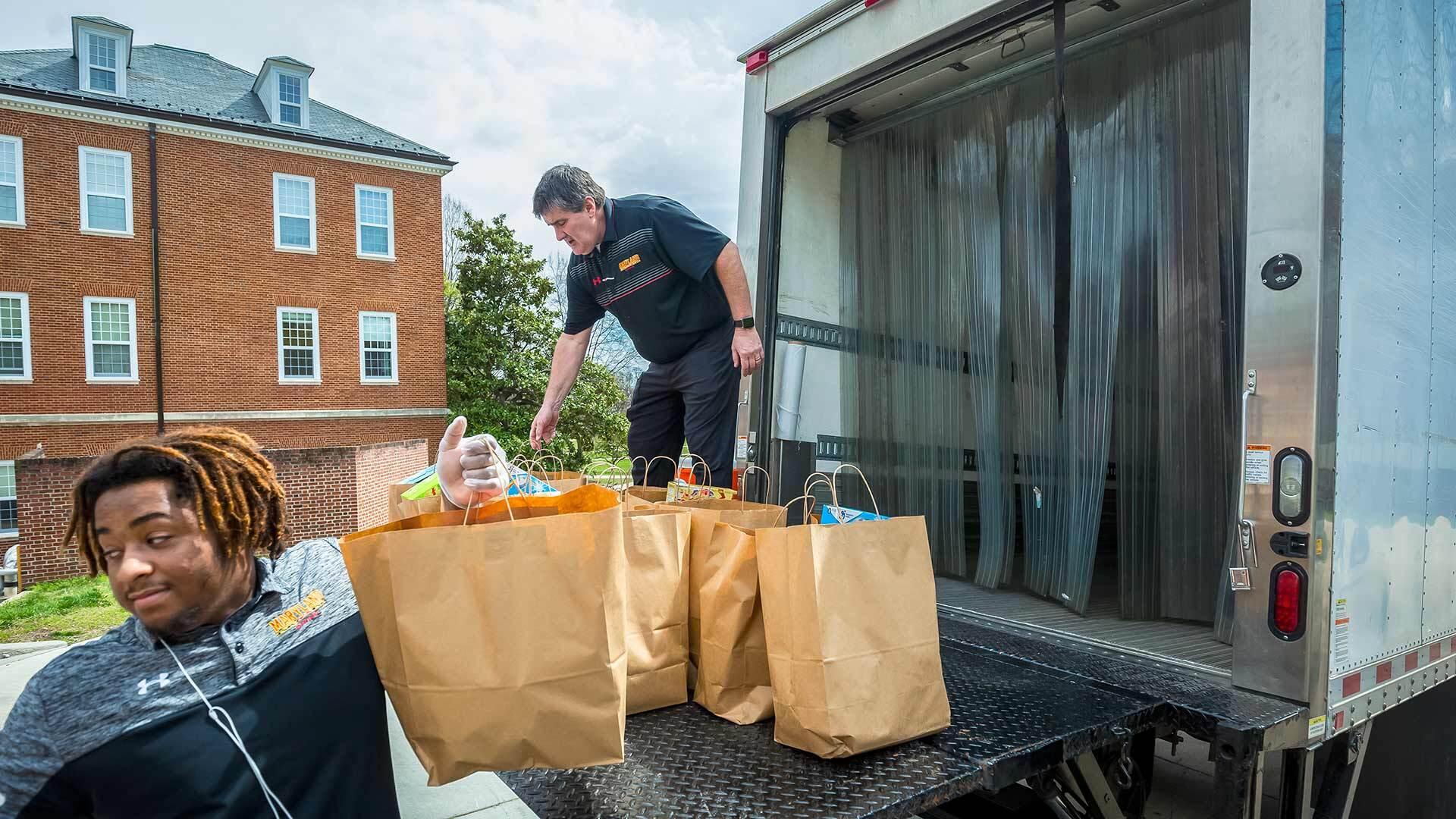 Two people unload bags of groceries from the back of a large shipping truck