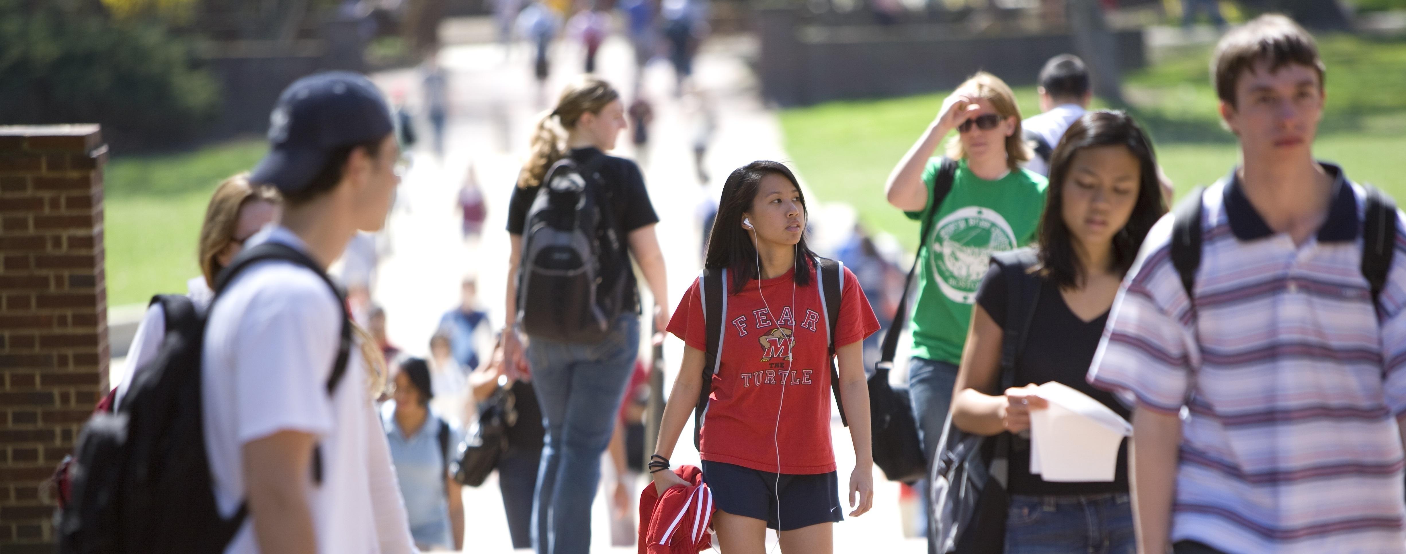 Female students wearing a red 'Fear the Turtle' tshirt walking in a crowd of people on the sidewalk near the Mall.