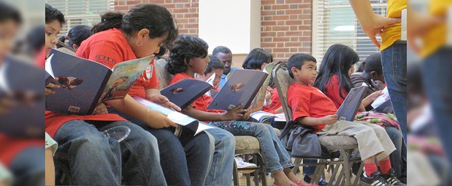 A crowd of children and some mentors seated in chairs, each holding the same book, with maracas on the cover