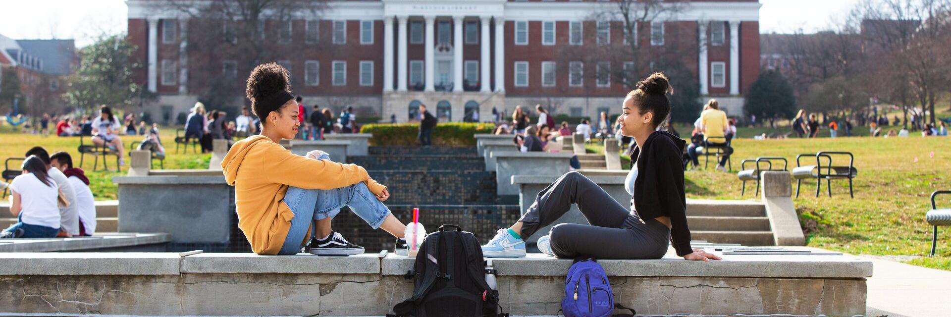 Two students sit facing each other on the ODK Fountain on McKeldin Mall