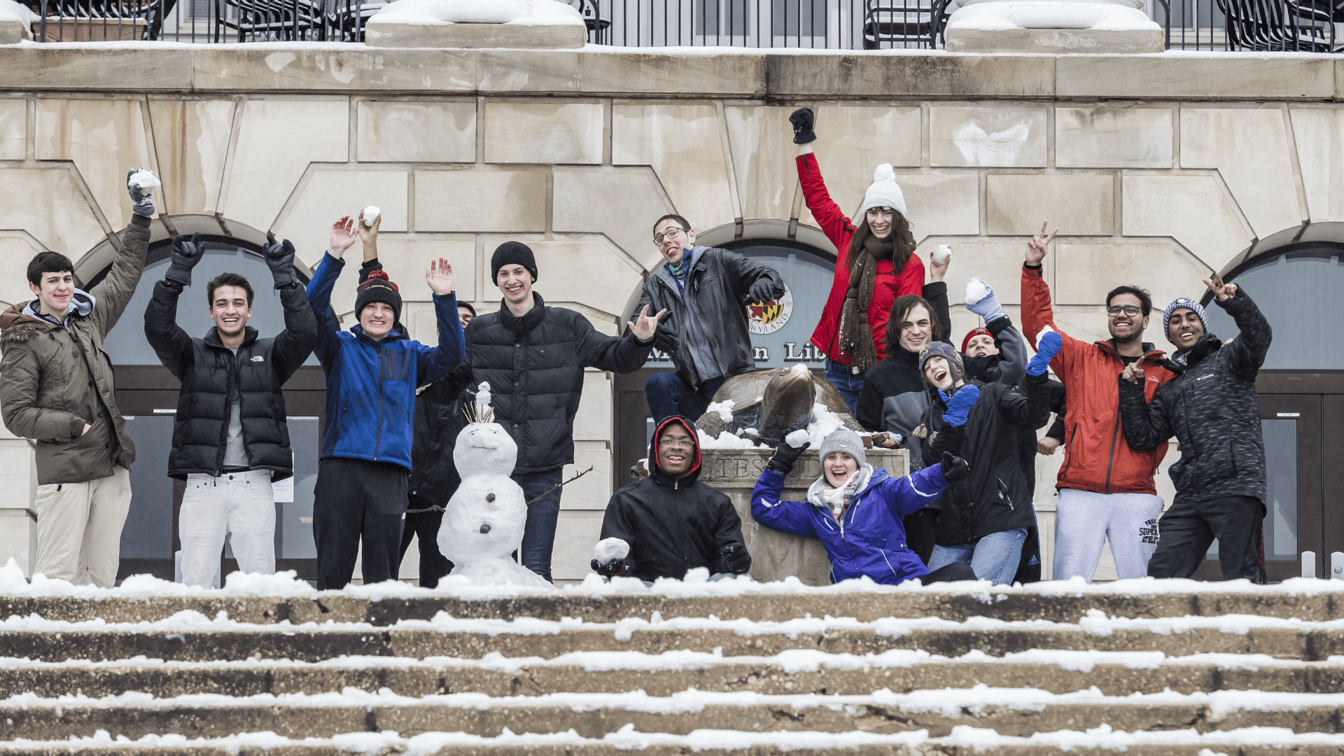 Students celebrate a snow day with snow balls held high on the steps of McKeldin Library