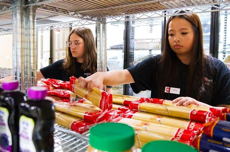 Two students stock shelves with pasta and dry goods at the UMD Campus Pantry.