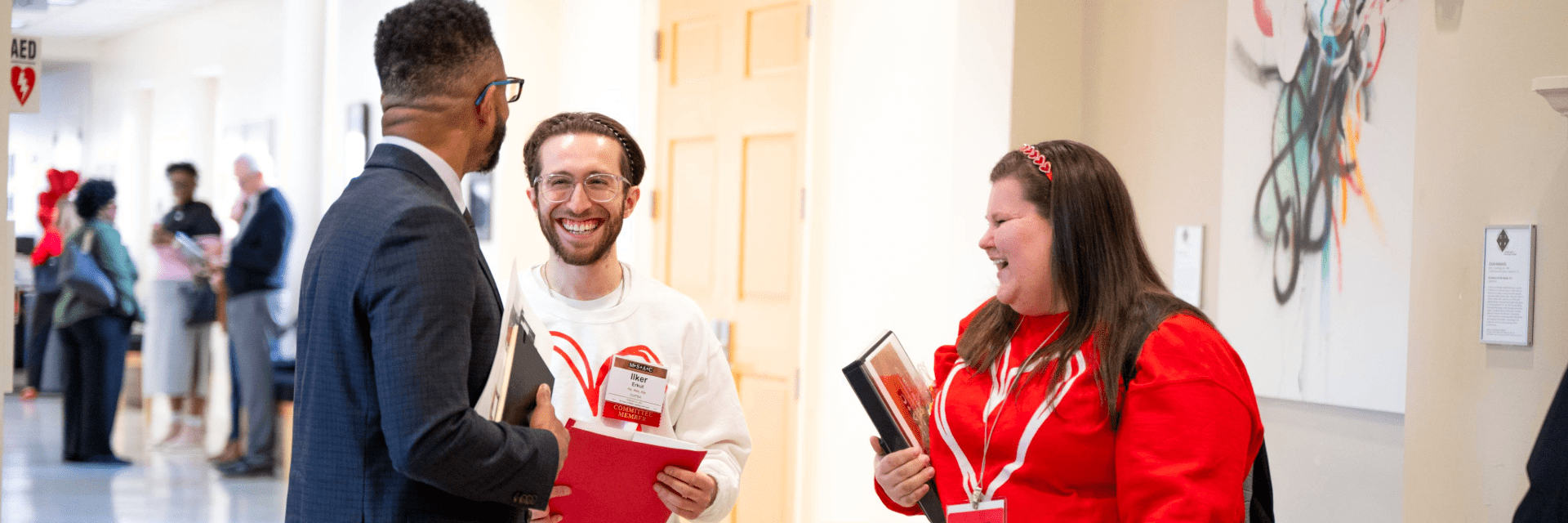 Three Student Affairs colleagues laugh and talk together in a hallway while holding notebooks and folders.