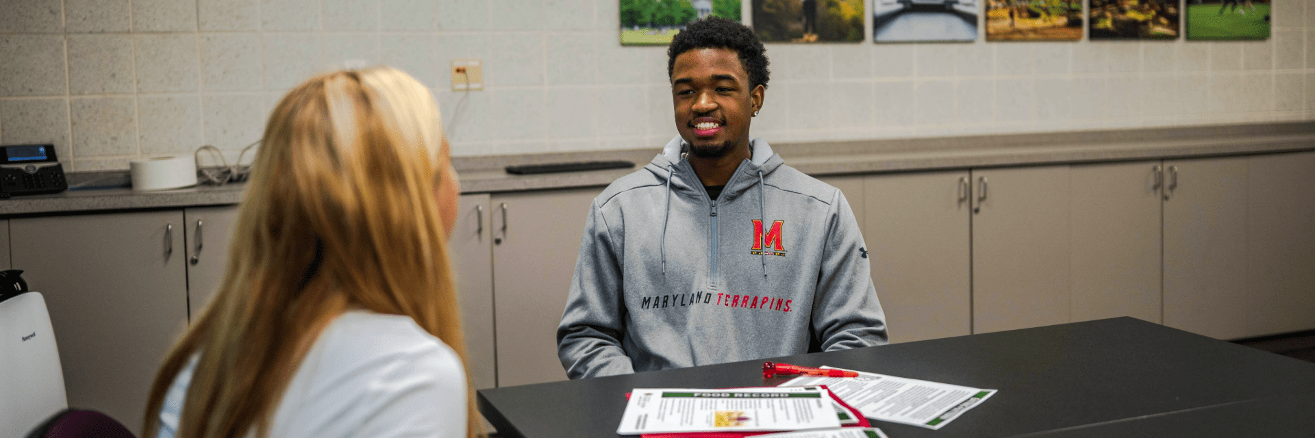 A student wearing a Maryland Terrapins hoodie smiles while meeting with a nutritionist.