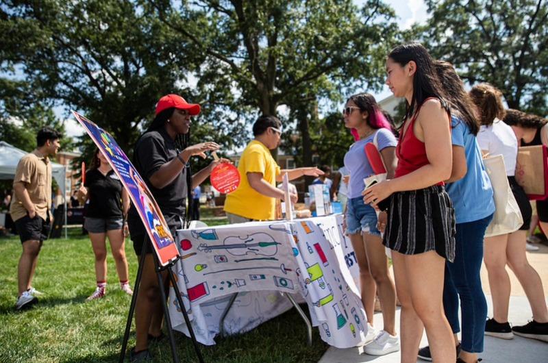 Students at an outdoor campus fair talking to representatives at a table.