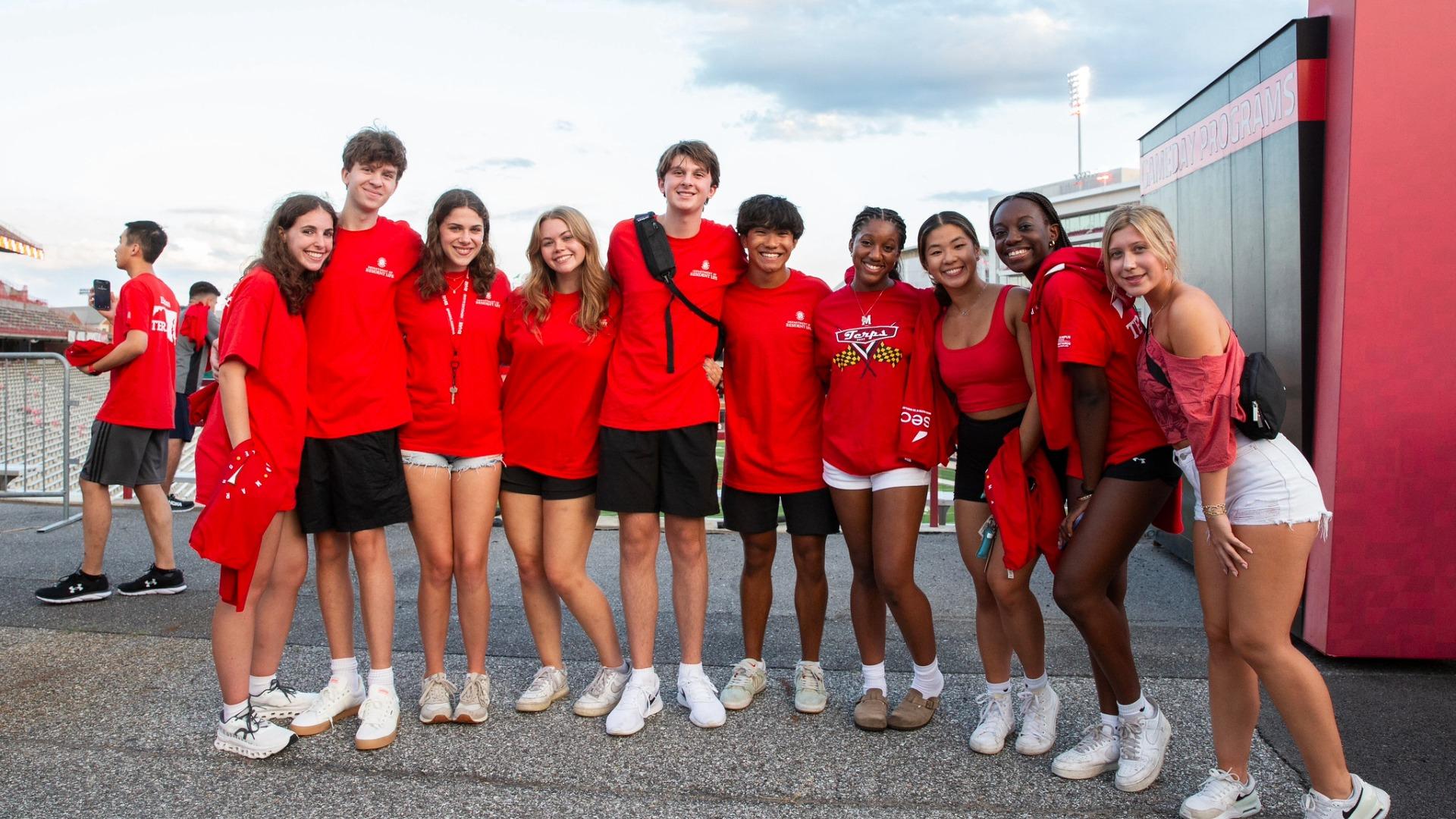 A group of smiling students in red Maryland apparel posing together at a SECU stadium.